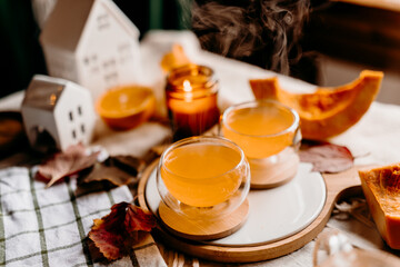 Two bright orange cups of pumpkin tea steaming in gentle autumn light. Cozy home comfort and relaxation mood.