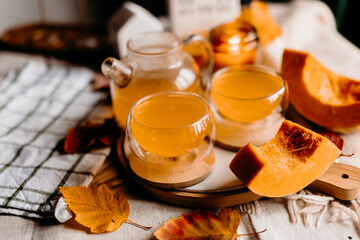Warm fall still life with two steaming orange pumpkin teas, autumn leaves and candles. Cozy seasonal home vibe.