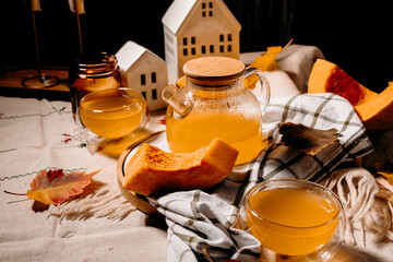 Transparent teapot with steaming pumpkin tea surrounded by candles and autumn leaves.