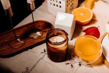Still life with burning candle in black glass and tea among autumn leaves. Cozy fall atmosphere and soft lighting.