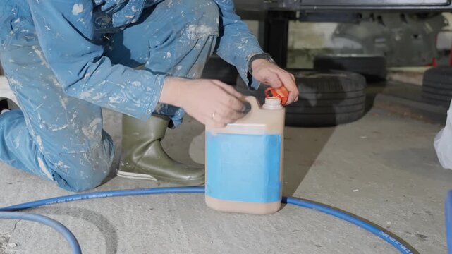 Man in workshop coveralls opens bottle of lanolin undercoating rust treatment and wipes finger to show non toxic formula.