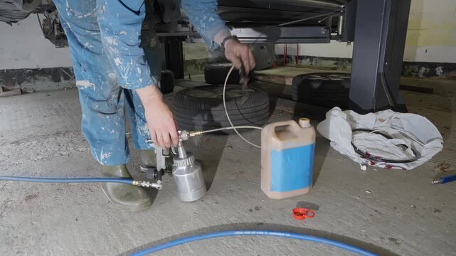 Man in workshop prepares to fill spray gun with natural lanolin rust treatment product used to protect car undercarriage.