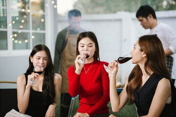 Three young women enjoying red wine together at a cozy outdoor party, smiling and relaxing with friends in a warm, festive atmosphere.