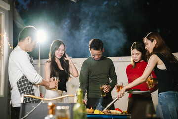 Group of friends having a fun backyard barbecue party at night, grilling food, chatting, and enjoying drinks together in a joyful atmosphere.