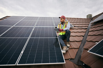 Electrical engineer working on touchpad while testing installed photovoltaic solar panels on roof. © Drazen