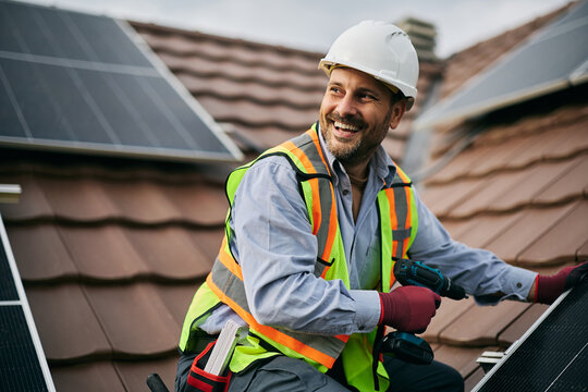 Happy worker mounting solar system on roof of residential building.