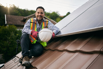 Happy technician mounting solar panel system on roof and looking at camera. © Drazen