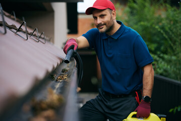 Close up of man using leaf blower while cleaning gutters on roof of house.