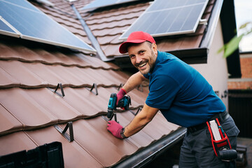 Happy worker installing snow guards on rooftop tiles and looking at camera