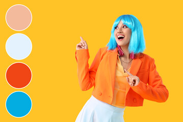 Beautiful young happy woman in blue wig pointing at something on yellow background