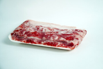 Two vacuum-sealed packages of thinly sliced raw beef on white styrofoam trays, with one in the foreground and the other slightly blurred in the background, isolated against a clean white surface.
