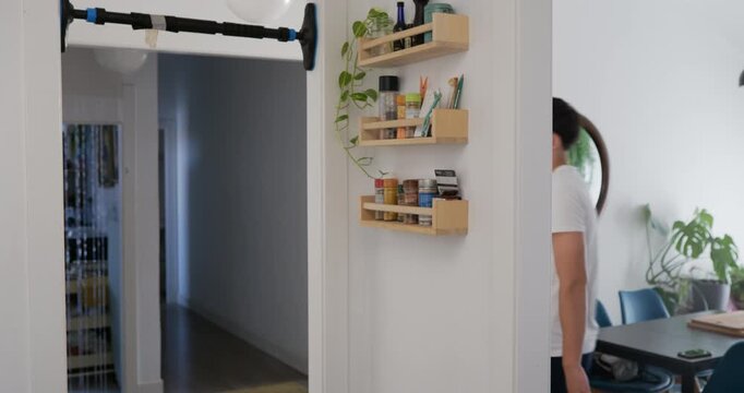 The lad goes into the kitchen, grabs a piece of pear and eats it, then hangs from a pull-up bar.