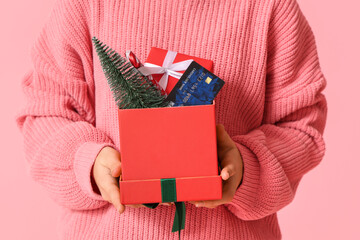 Girl with gift boxes, credit card and Christmas tree on pink background, closeup