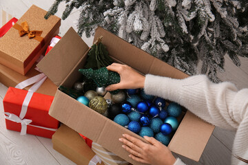 Woman putting Christmas toys in  cardboard box at home, closeup © Pixel-Shot