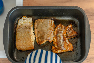 A hand in a potholder holds a pan of fried fish