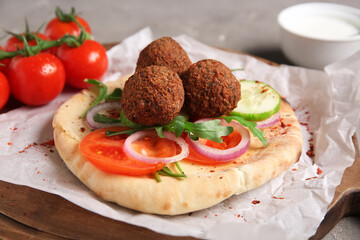 Wooden board of delicious pita with falafel and fresh vegetables on grey background, closeup