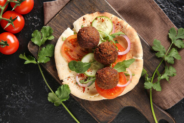 Wooden board of delicious pita with falafel and fresh vegetables on black background