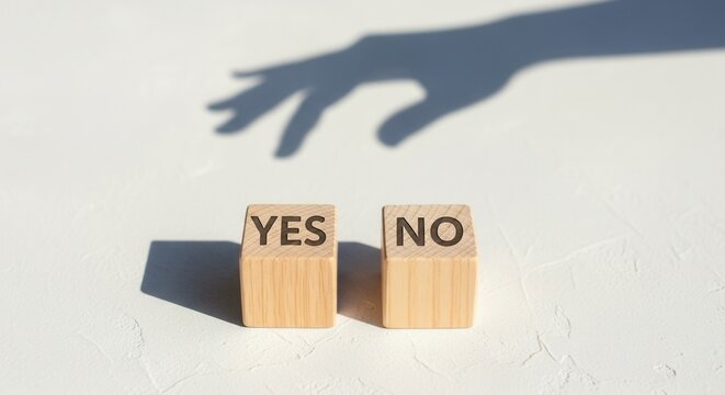 A hand shadow reaches towards two wooden blocks labeled YES and NO on a textured light-colored surface with harsh shadows - Powered by Adobe