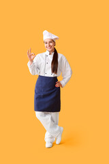 Young female chef showing ok gesture on yellow background