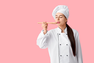 Young female chef with wooden spoon on pink background
