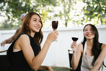 Group of friends enjoying barbecue and wine together in a cozy outdoor party, smiling and chatting in a cheerful atmosphere.