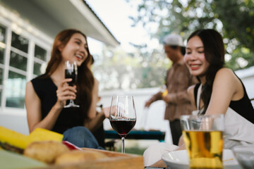 Group of friends enjoying barbecue and wine together in a cozy outdoor party, smiling and chatting in a cheerful atmosphere.