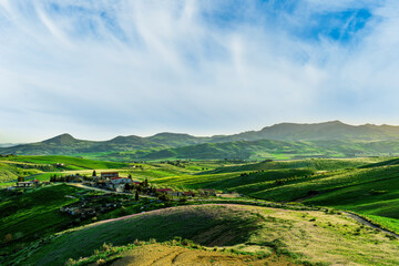 amazing greeen hills and fields in a spring or summer rustic landscape with rustic village on agricultural hills with beautiful colorful sky and mountains