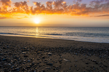 morning landscape with coast on foreground, sand of a beach, blue sea with surf and waves and cloudy sunset or sunrise on background