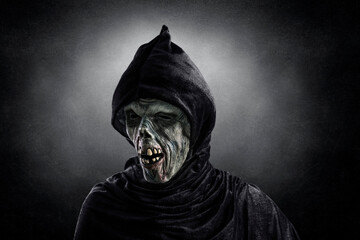 Portrait of a zombie with hooded cape over dark misty background