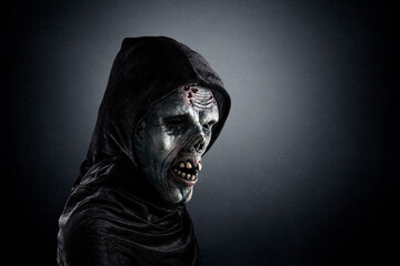Portrait of a zombie with hooded cape over dark misty background
