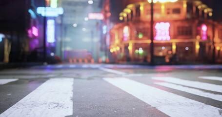 Bright neon signs reflect on a wet street surface in a city at night. The atmosphere suggests a calm yet lively urban setting with colorful lights around.