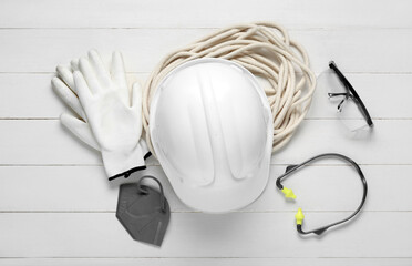 Hardhat with safety equipment on white wooden background