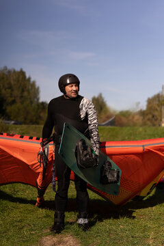 Man in wetsuit holding kiteboard standing in front of kite