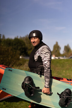Man in wetsuit holding kiteboard standing in front of orange kite