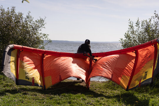 Kiteboarder preparing orange and yellow kite on grassy shore