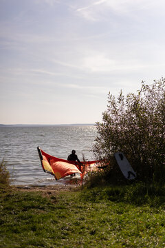 Kiteboarder preparing orange and yellow kite on grassy shore