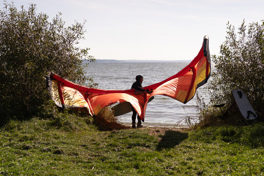 Kiteboarder preparing orange and yellow kite on grassy shore