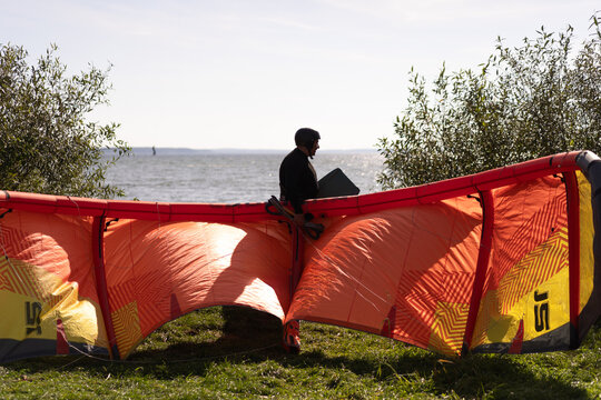Kiteboarder preparing orange and yellow kite on grassy shore