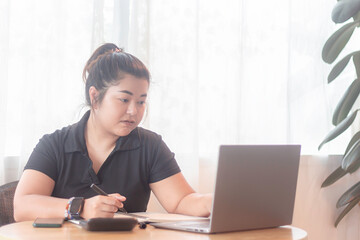 Young woman working from home at a wooden desk with a laptop and notebook near a window on a bright day