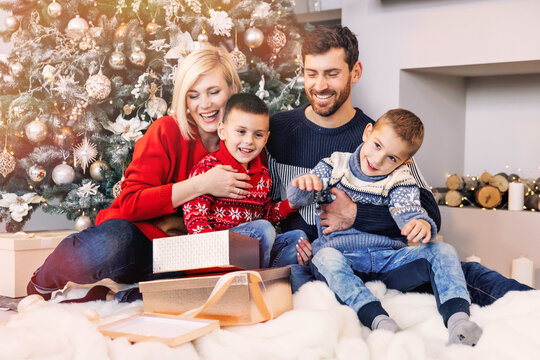 Cheerful family with mother and father and two sons open gift boxes for christmas while sitting on the floor