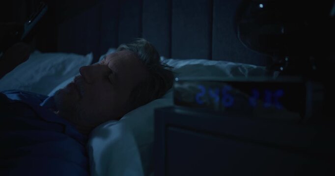 Close Up of Middle Aged Man in Pajamas Lying in Bed at Two AM, Scrolling Smartphone. Concept of Insomnia, Unhealthy Digital Habits, Late Night Stress, Sleep Disorder, and Dependence on Technology.