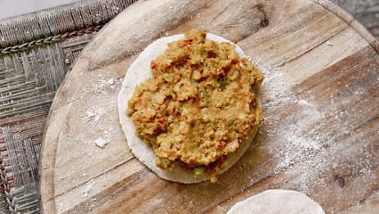 Circular flatbread with filling on wooden board, flour dusted surface