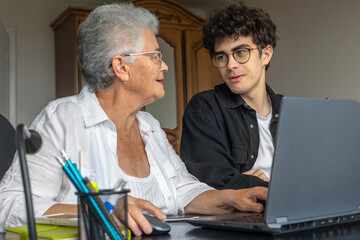 Teenage grandson teaching his grandmother to use a laptop at home. Generations learning together, family support, digital literacy for seniors, technology, connection, love, and intergenerational care