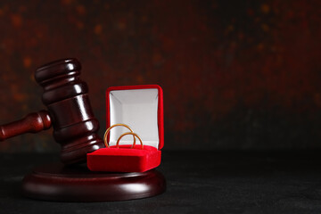 Judge's gavel with box of wedding rings on black table near grunge wall