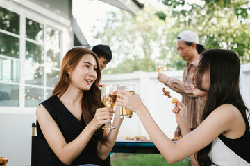 Group of friends enjoying barbecue and wine together in a cozy outdoor party, smiling and chatting in a cheerful atmosphere.