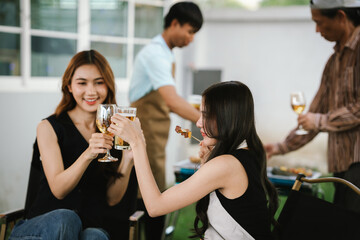 Group of friends enjoying barbecue and wine together in a cozy outdoor party, smiling and chatting in a cheerful atmosphere.