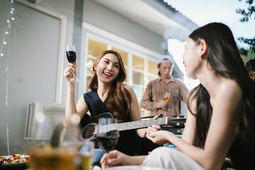 Group of friends enjoying barbecue and wine together in a cozy outdoor party, smiling and chatting in a cheerful atmosphere.