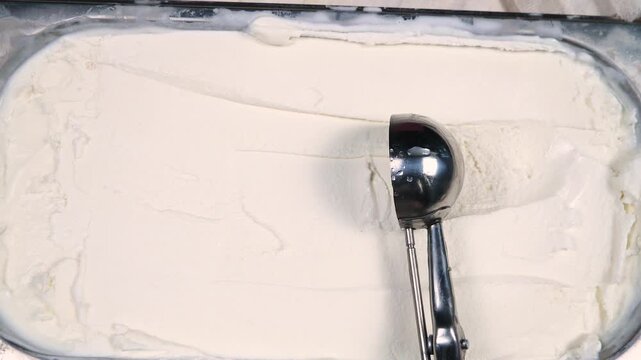 Scoops of vanilla ice cream are slowly placed on a spoon and removed from the container.