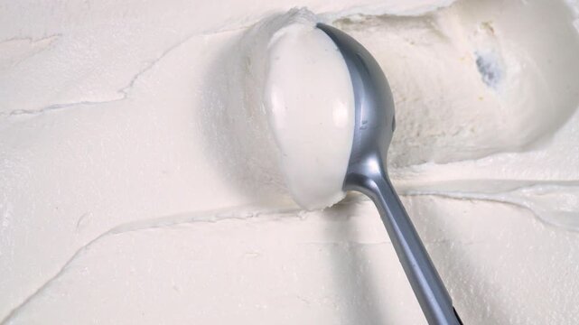 Scoops of vanilla ice cream are slowly placed on a spoon and removed from the container.