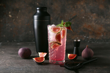 Glass of tasty fig lemonade and bartender tools on brown grunge background, closeup